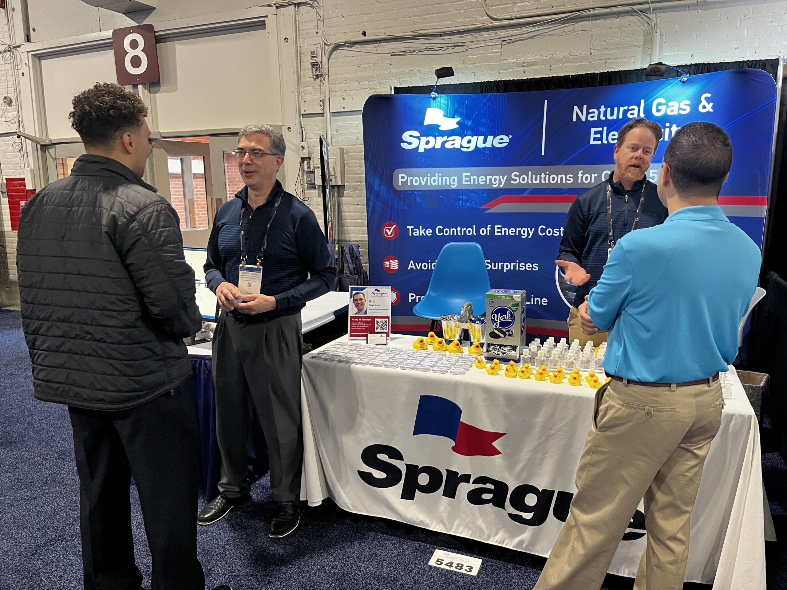 Sprague team members speaking with attendees at a trade show booth promoting natural gas and electricity solutions.