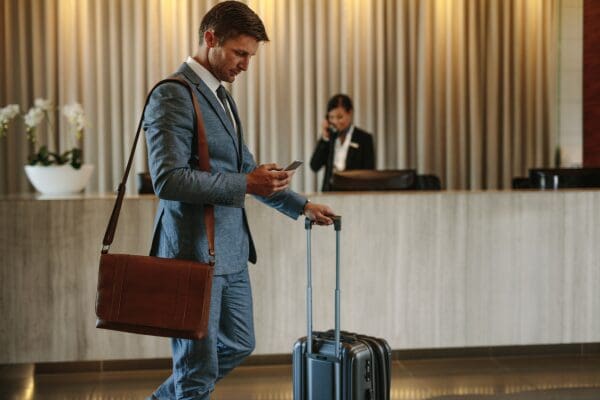 Hotel guest checking a phone while standing with luggage at a front desk.