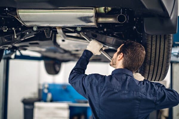 Automotive technician inspecting the underside of a vehicle in a service bay.