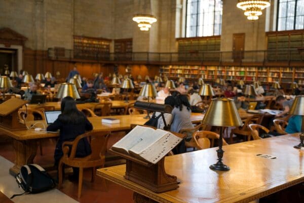 Students studying at desks inside a large academic library reading room in an educational institution